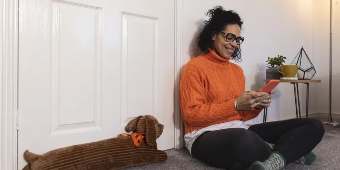 A person in an orange jumper smiles whilst looking at their phone, near a dog shaped draught excluder