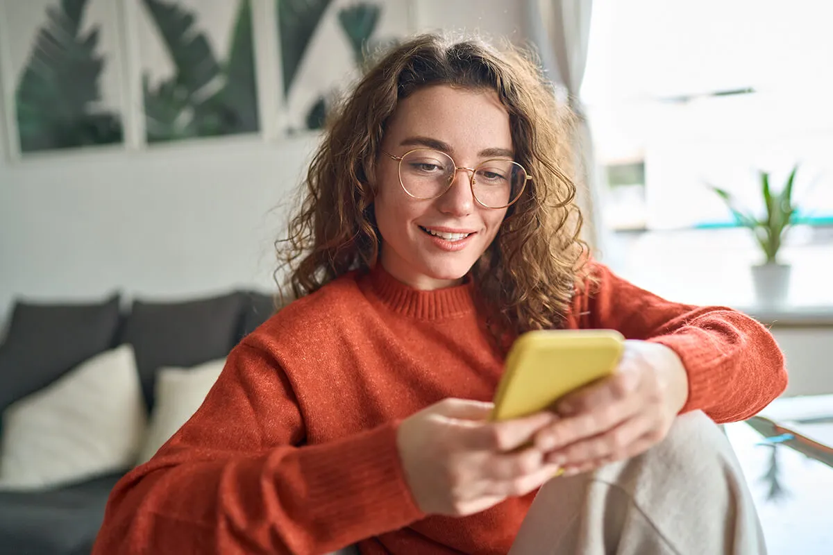 Girl wearing orange jumper sitting down looking at her phone and smiling