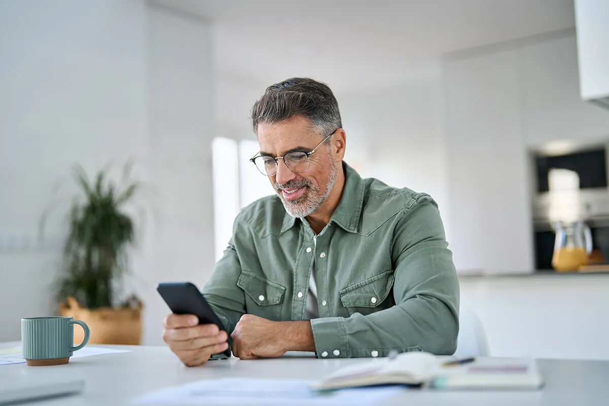 Smiling person wearing glasses and a green overshirt uses their phone