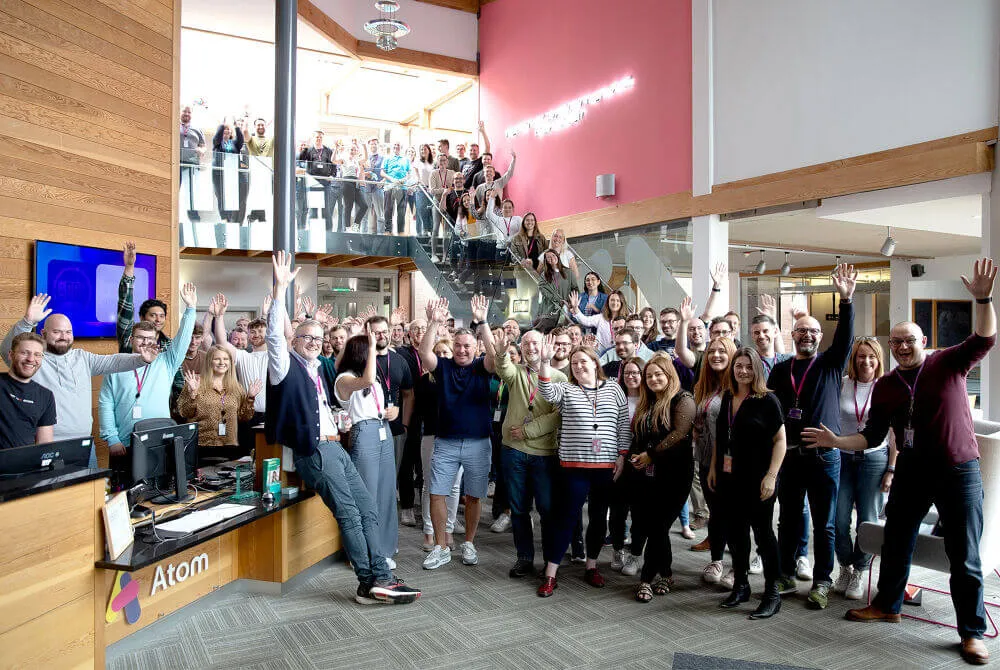 Many Atom bank staff gathered in the reception area, waving and smiling, at Atom headquarters