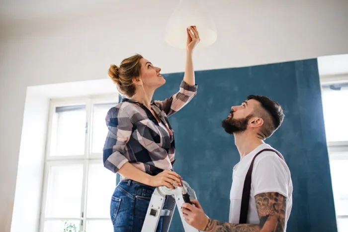 Two people use stepladder to change a lightbulb